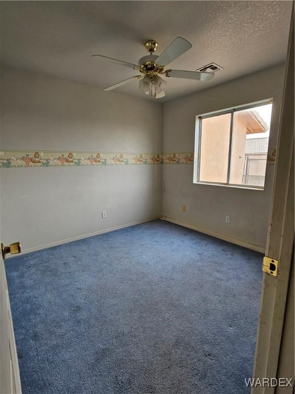 carpeted spare room featuring a textured ceiling, baseboards, visible vents, and a ceiling fan