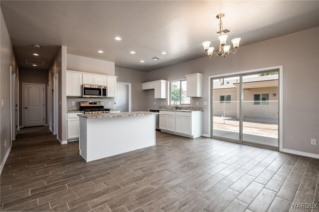 kitchen featuring visible vents, a kitchen island, decorative light fixtures, stainless steel appliances, and white cabinetry