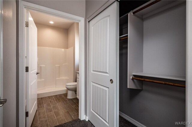 full bathroom featuring a walk in closet, toilet, wood tiled floor, a shower stall, and baseboards