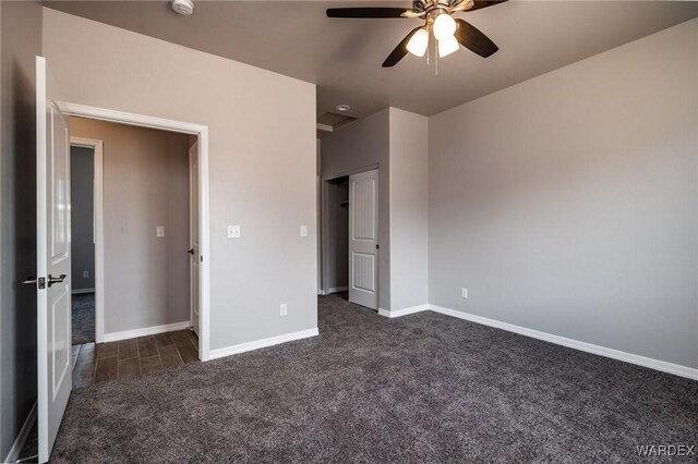 unfurnished bedroom with baseboards, dark colored carpet, and a ceiling fan