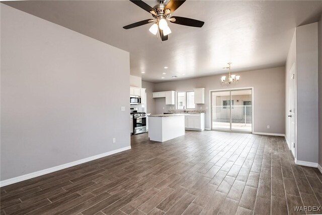 unfurnished living room with recessed lighting, ceiling fan with notable chandelier, dark wood-style flooring, a sink, and baseboards