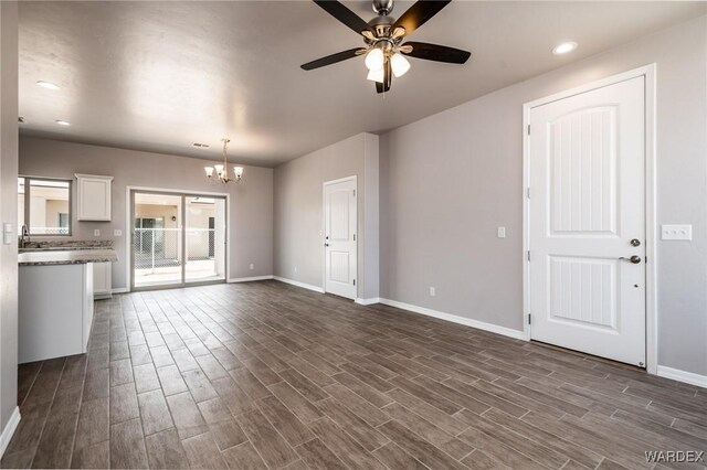 unfurnished living room featuring ceiling fan with notable chandelier, dark wood-style flooring, recessed lighting, and baseboards