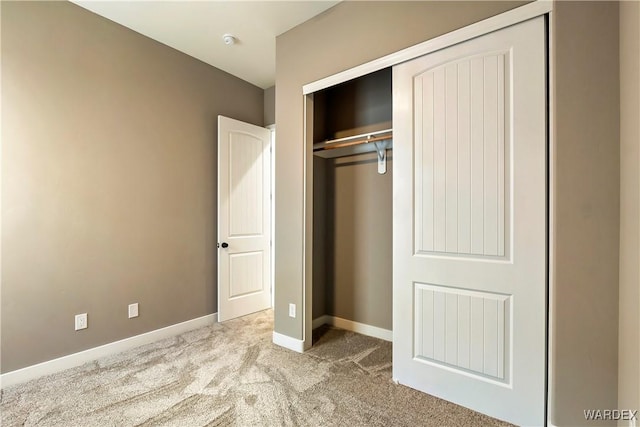 unfurnished bedroom featuring baseboards, a closet, and light colored carpet