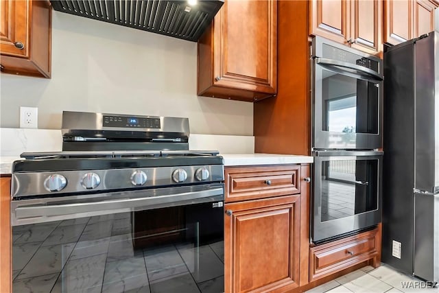 kitchen with marble finish floor, appliances with stainless steel finishes, brown cabinetry, and exhaust hood