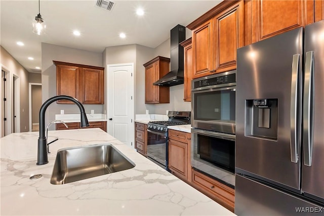 kitchen with stainless steel appliances, wall chimney exhaust hood, light stone countertops, and pendant lighting