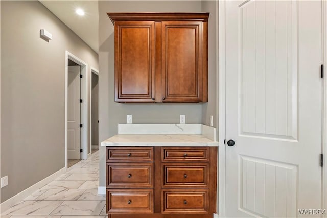 kitchen with light stone countertops, marble finish floor, baseboards, and brown cabinetry