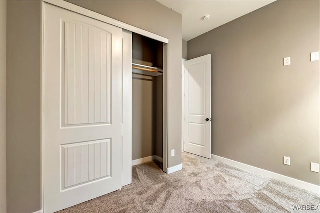 unfurnished bedroom with a closet, light carpet, and baseboards