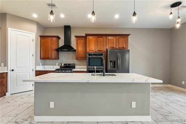 kitchen with appliances with stainless steel finishes, brown cabinets, a center island with sink, and wall chimney exhaust hood