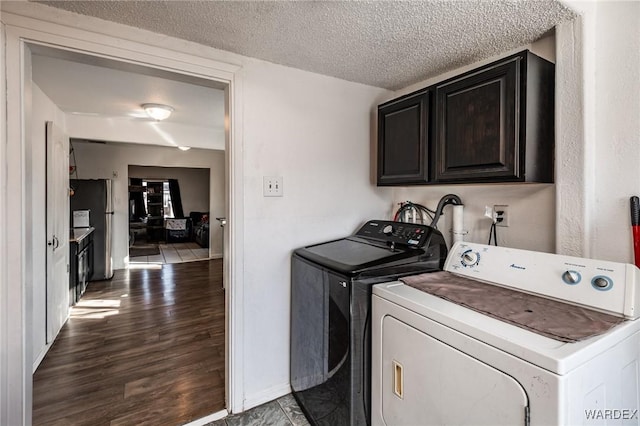 washroom with cabinet space, a textured ceiling, dark wood-type flooring, and washer and dryer