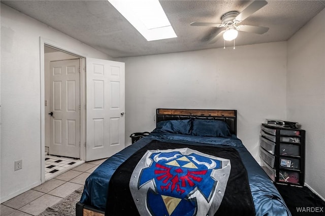 bedroom with a skylight, ceiling fan, a textured ceiling, and tile patterned floors