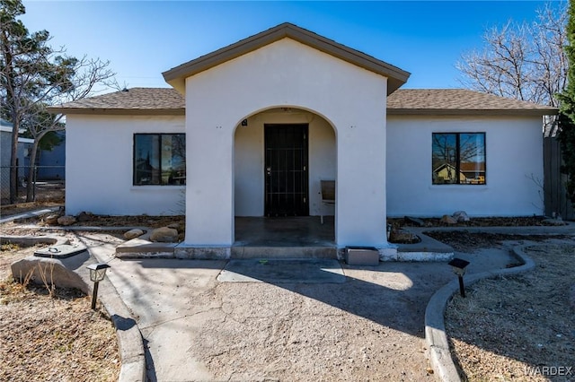 view of front facade with a shingled roof, a patio area, and stucco siding