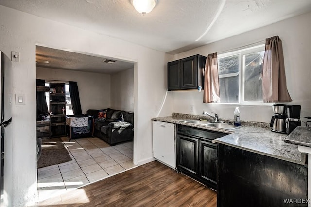 kitchen featuring visible vents, a sink, light wood-type flooring, dark cabinetry, and dishwasher