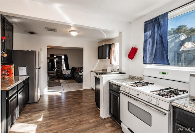 kitchen with dark wood-style flooring, visible vents, freestanding refrigerator, dark cabinetry, and white gas range oven