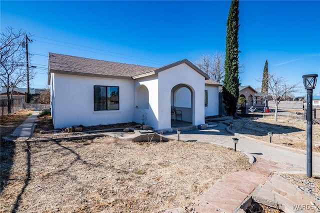 view of front of home featuring roof with shingles, fence, and stucco siding