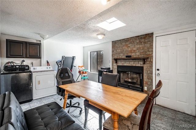 dining area with a textured ceiling, a brick fireplace, washing machine and dryer, and light tile patterned flooring