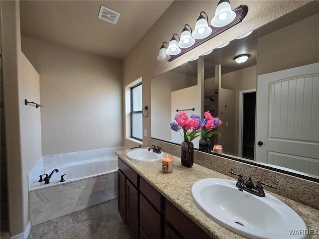 bathroom with a bath, double vanity, visible vents, and a sink