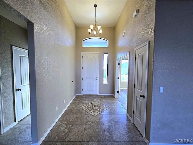 foyer with an inviting chandelier, baseboards, and a textured wall