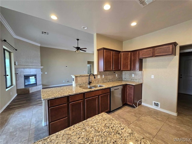 kitchen with a tiled fireplace, a sink, light stone countertops, dishwasher, and a peninsula