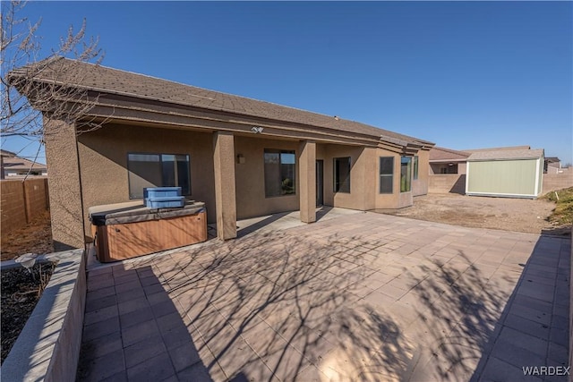 rear view of house featuring a fenced backyard, stucco siding, a shed, a patio area, and a hot tub