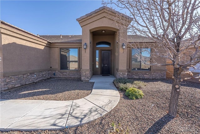 property entrance with stone siding, a tile roof, and stucco siding