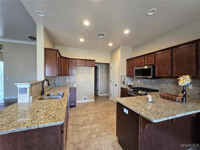 kitchen with a peninsula, light stone countertops, appliances with stainless steel finishes, and a sink