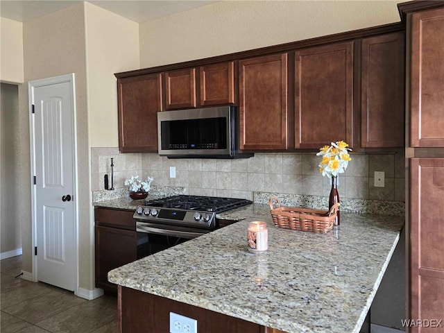 kitchen with stainless steel appliances, decorative backsplash, light stone counters, and dark brown cabinets