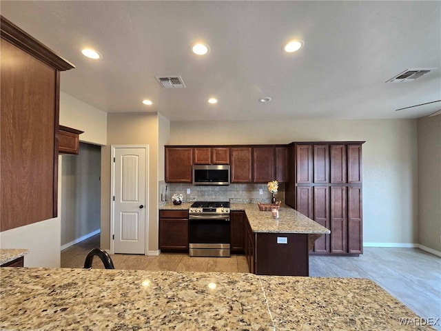 kitchen with stainless steel appliances, light stone counters, visible vents, and tasteful backsplash