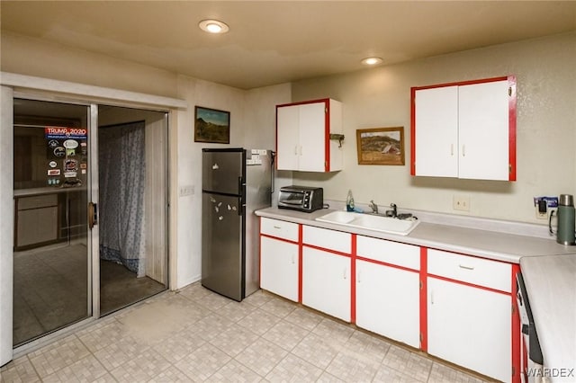 kitchen with a toaster, light countertops, freestanding refrigerator, white cabinets, and a sink