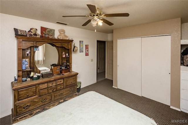 bedroom with a textured ceiling, visible vents, a ceiling fan, a closet, and dark colored carpet