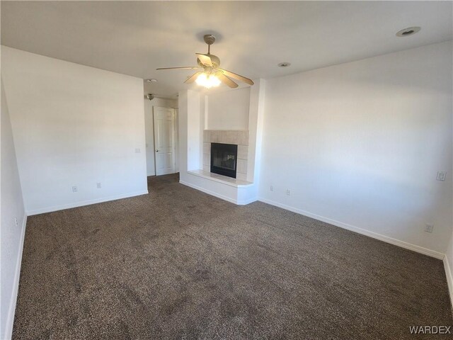 unfurnished living room with a tiled fireplace, dark carpet, a ceiling fan, and baseboards