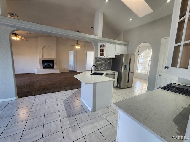 kitchen featuring arched walkways, stainless steel appliances, glass insert cabinets, white cabinets, and a sink