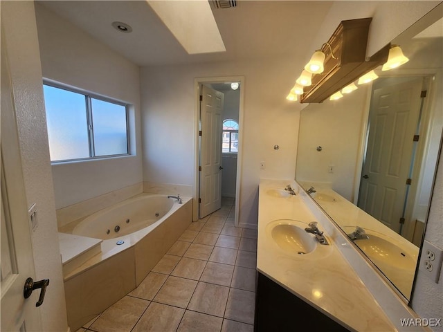 bathroom with double vanity, a tub with jets, a sink, and tile patterned floors