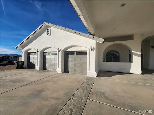 exterior space featuring driveway, an attached garage, and stucco siding