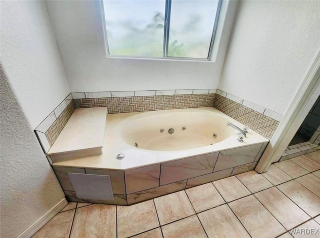 bathroom with tile patterned flooring, a textured wall, and a tub with jets