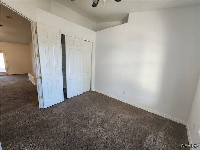 unfurnished bedroom with baseboards, dark colored carpet, and a closet