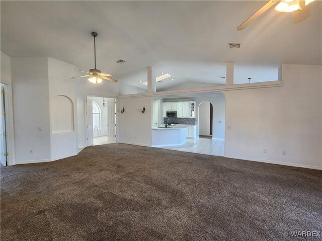 unfurnished living room with light carpet, arched walkways, visible vents, and a ceiling fan