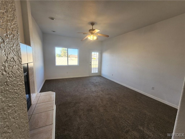 unfurnished living room featuring dark colored carpet, ceiling fan, and baseboards