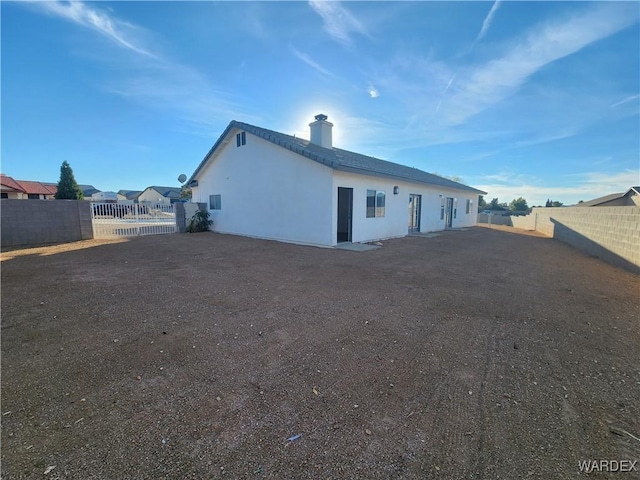 rear view of property featuring a chimney, a fenced backyard, and stucco siding