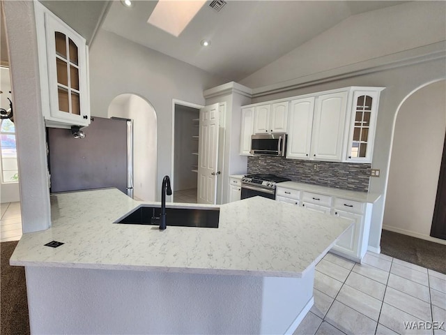 kitchen with arched walkways, white cabinets, appliances with stainless steel finishes, glass insert cabinets, and a sink