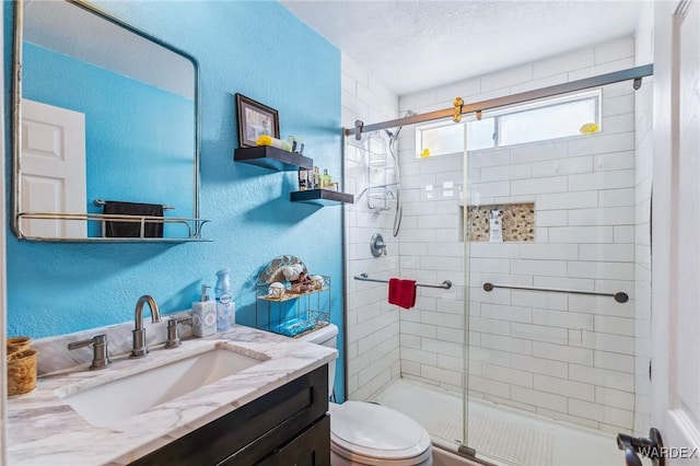 bathroom featuring a textured ceiling, a textured wall, toilet, vanity, and a shower stall