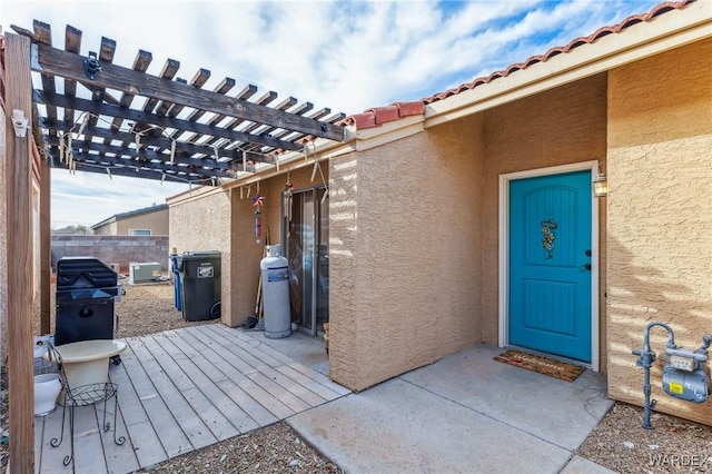 view of exterior entry with a pergola, fence, a tile roof, and stucco siding