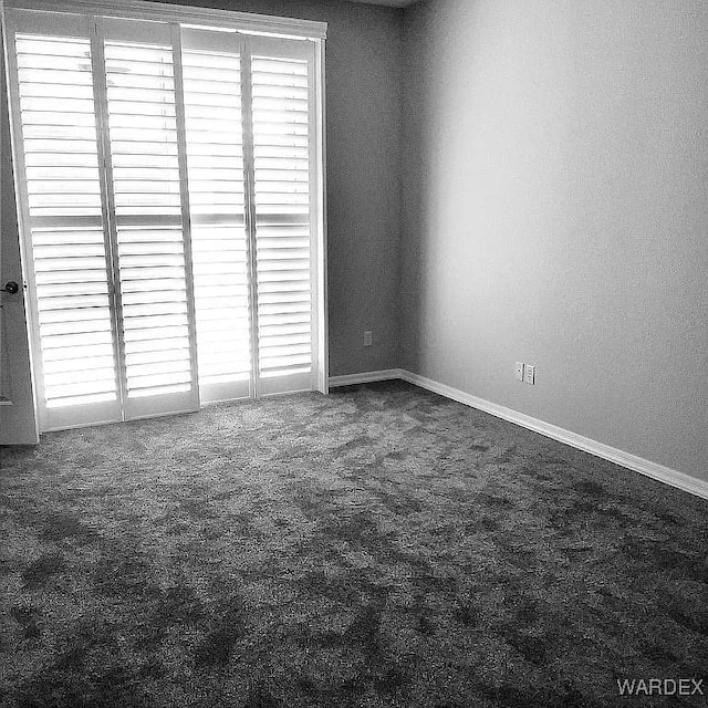 empty room featuring dark colored carpet and baseboards