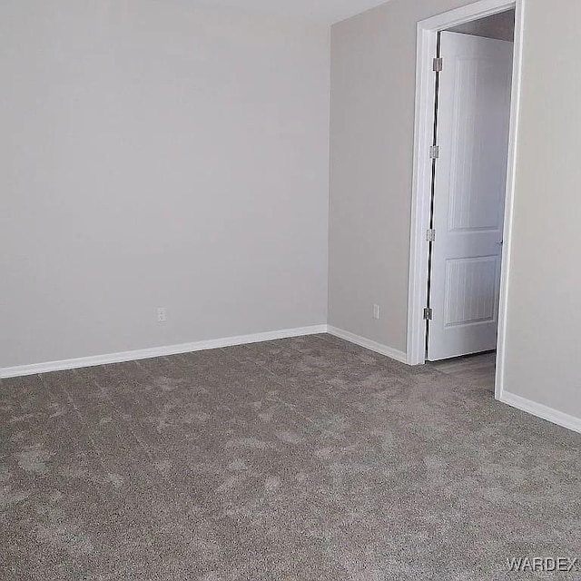 spare room featuring dark carpet and baseboards