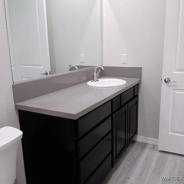 bathroom featuring toilet, vanity, baseboards, and wood finished floors