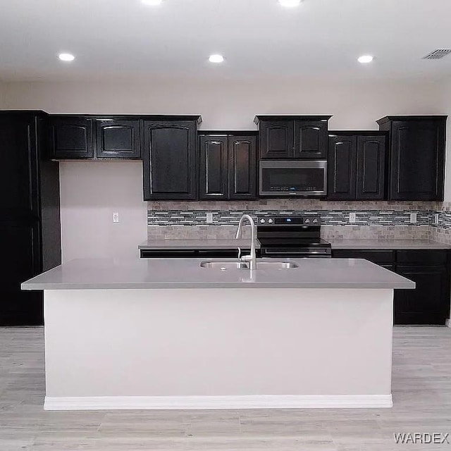 kitchen featuring a sink, a kitchen island with sink, stainless steel microwave, and electric stove