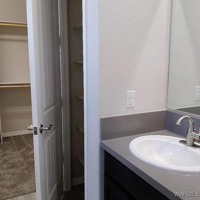 bathroom featuring a walk in closet, a textured wall, and vanity