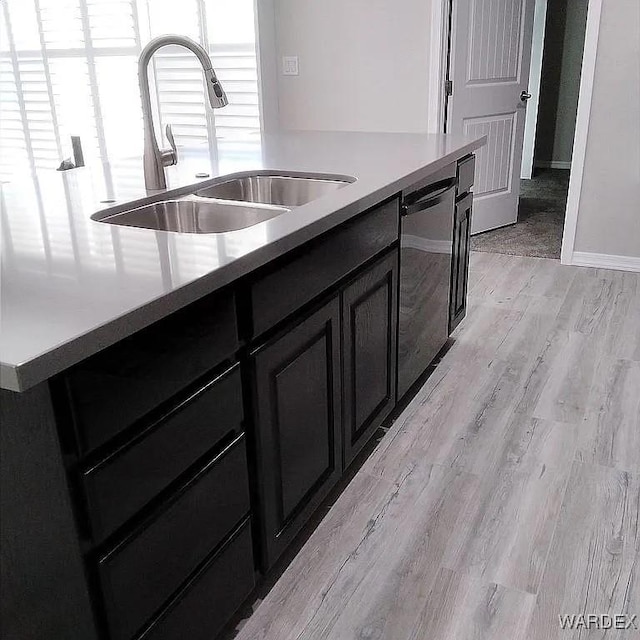 kitchen featuring dishwashing machine, light wood-style flooring, dark cabinets, light countertops, and a sink