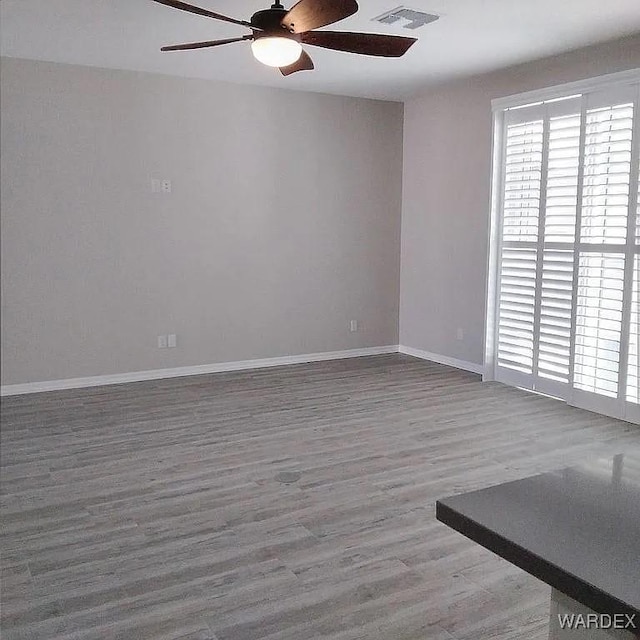 spare room with a ceiling fan, wood finished floors, visible vents, and baseboards