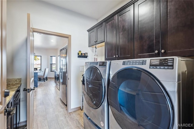 laundry area featuring separate washer and dryer, light wood-style flooring, cabinet space, and baseboards