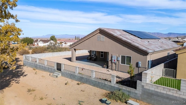 view of side of property with fence private yard, a mountain view, solar panels, stucco siding, and a patio area